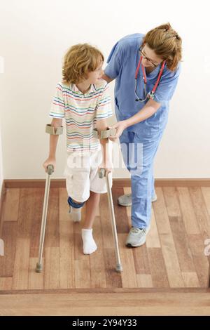 Enfant blessé sur béquilles. Garçon en plâtre sur le pied et la jambe. Petit enfant avec une ancle entorse apprenant à marcher à nouveau. Physiothérapie en clinique de santé. Banque D'Images