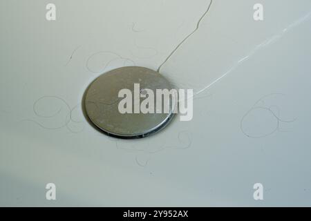 Un drain de douche avec de l'eau coulant dans le trou. Poils errants ! Cheveux dans la douche. Banque D'Images