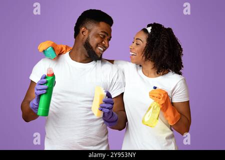 Prêt pour le nettoyage. Couple de Noirs heureux avec des outils ménagers sur fond rose Banque D'Images