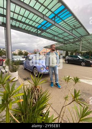 Homme debout devant une voiture violette vintage dans la rue en été. Nostalgie à l'ancienne et concept de style rétro Banque D'Images