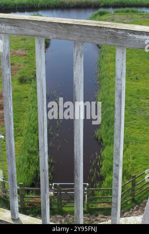 Une vue vers le bas depuis le dernier étage de Horsey Windpump, à travers le rail de clôture en bois jusqu'au canal d'eau et l'herbe ci-dessous, Norfolk, Angleterre Royaume-Uni Banque D'Images