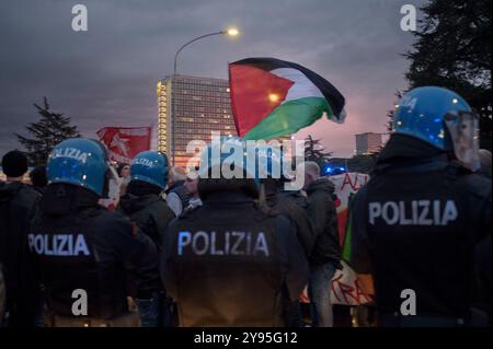 Rome, Italie. 8 octobre 2024. Des policiers en tenue anti-émeute alors que des étudiants de collectifs palestiniens agitent le drapeau palestinien lors d'une manifestation contre les entreprises qui travaillent avec Israël lors de la conférence 'Cybertech Europe 2024'' à Rome. Quelques dizaines d'étudiants appartenant aux collectifs d'étudiants pour la Palestine avaient exprimé leur intention de marcher devant le Fuksas Nuvola Congress Center où se déroule la conférence ''Cybertech Europe 2024'', avec la participation de certaines entreprises ayant des collaborations avec des entreprises israéliennes. Sans incident, ils ont plutôt été escortés par le Banque D'Images