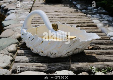 Sur un pont en bois pittoresque, se trouve un panier magnifiquement conçu qui est en forme de cygne blanc gracieux, créant une scène élégante Banque D'Images