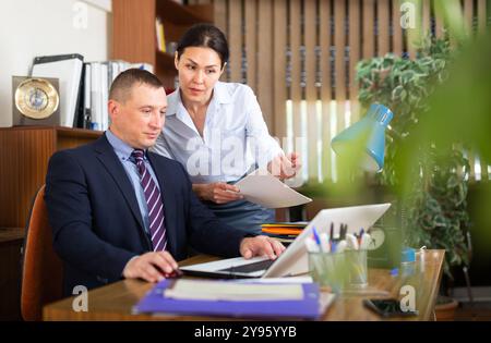 Homme d'affaires avec une collègue féminine travaillant avec un ordinateur portable et des papiers Banque D'Images