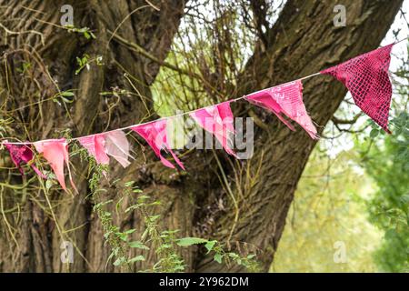 Guirlande avec des drapeaux de déchets de tissu rose suspendus dans un arbre lors d'une fête dans le jardin ou le parc, mise au point sélectionnée, profondeur de champ étroite Banque D'Images