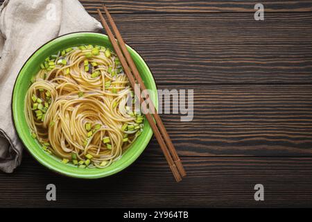 Soupe de nouilles asiatiques dans un bol en céramique rustique vert avec des baguettes en bois vue de dessus sur fond en bois foncé. Nouilles LO mein avec bouillon et oni vert Banque D'Images