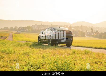 SUV conduite sur une route de campagne avec vue sur une ville au coucher du soleil, VW ID5 voiture électrique, Calw, Forêt Noire, Allemagne, Europe Banque D'Images