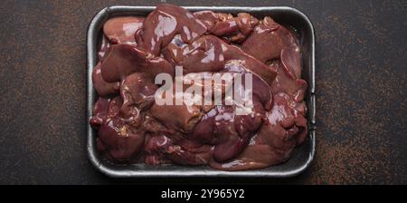 Foie de poulet cru dans le plateau de supermarché noir vue sur fond de béton rustique foncé table de cuisine. Ingrédient alimentaire sain, source de fer, folate Banque D'Images