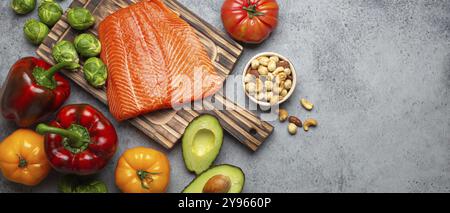 Filet de saumon cru frais sur planche à découper en bois, légumes bio biologiques et noix sur fond gris pierre rustique vue de dessus. Ingrédients pleins de vitamines Banque D'Images