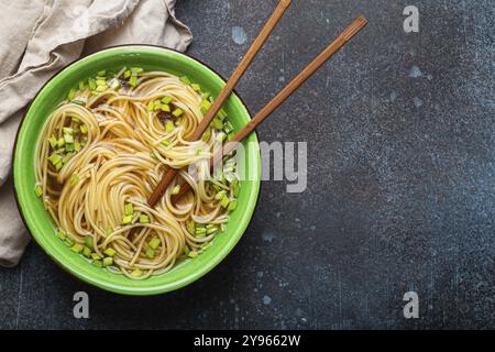 Soupe de nouilles asiatiques dans un bol en céramique rustique vert avec des baguettes en bois vue de dessus sur fond de pierre rustique. Nouilles LO mein au bouillon et vert Banque D'Images