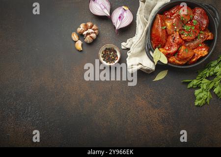 Cuisson d'un ragoût de viande copieux. Morceaux de viande hachés crus non cuits marinés avec assaisonnements et persil dans une casserole noire vue de dessus, ingrédients sur d Banque D'Images