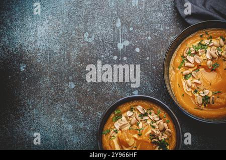 Un bol en céramique avec soupe à la crème de potiron décorée d'arachides sur fond de pierre sombre avec une cuillère décorée, par le dessus. Concept de dîner d'automne confortable, s Banque D'Images