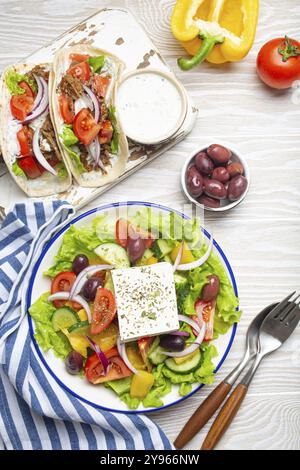 Cuisine grecque traditionnelle : salade grecque, Gyros avec viande et légumes, sauce Tzatziki, olives sur fond de table en bois rustique blanc vue de dessus. Cuisine Banque D'Images