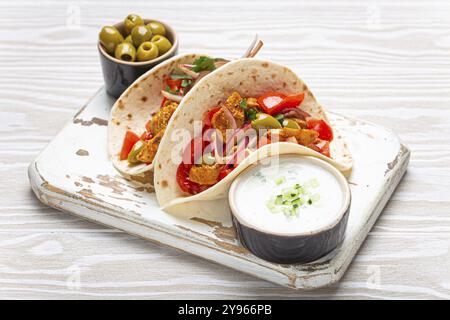 Cuisine grecque traditionnelle Gyros: Pain pita enveloppé de légumes, viande, herbes, olives sur une planche à découper rustique en bois avec sauce Tzatziki, huile d'olive Banque D'Images