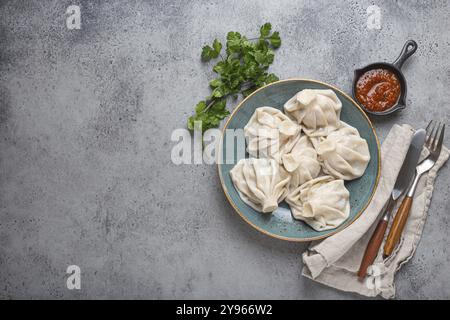 Boulettes géorgiennes Khinkali sur plaque avec sauce tomate rouge et coriandre fraîche vue de dessus sur fond de pierre rustique, plat traditionnel de Géorgie. Espace Banque D'Images