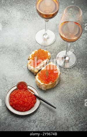 Petite assiette en métal avec caviar de saumon rouge, deux toasts de caviar canape, deux verres de champagne vue de dessus sur fond de béton gris, luxe festif del Banque D'Images