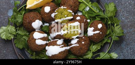 Assiette de boules de falafel frites servi avec coriandre verte fraîche et vue de dessus de citron sur fond de béton rustique. Plat végétalien traditionnel de Middle Easte Banque D'Images