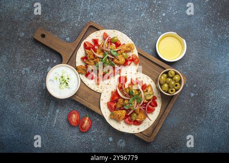 Cuisine traditionnelle grecque Gyros : pain pita avec des légumes, de la viande, des herbes, des olives sur une planche à découper rustique en bois avec sauce Tzatziki, huile d'olive à Banque D'Images