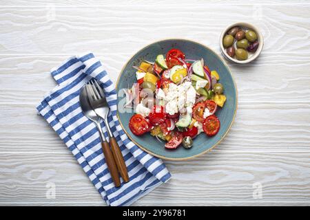 Salade grecque fraîche saine et colorée avec fromage feta, légumes, olives dans un bol en céramique bleue sur fond de bois blanc rustique vue sur le dessus, Méditerranée Banque D'Images