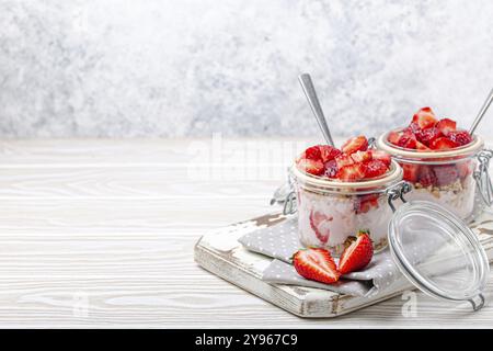 Parfait avec des fraises fraîches, yaourt et granola Crunchy en verre transparent Mason bocaux sur fond blanc rustique en bois vue d'angle, Healthy bre Banque D'Images