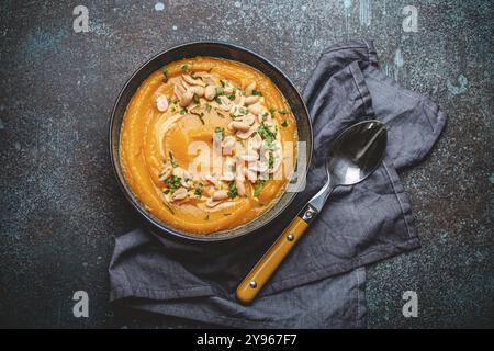 Un bol en céramique avec soupe à la crème de citrouille décorée avec des arachides sur fond de pierre sombre avec cuillère décorée, par le haut. Concept de dîner confortable d'automne, f Banque D'Images
