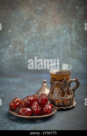 Rompre le jeûne avec des dattes séchées pendant le Ramadan Kareem, repas d'iftar avec des dattes et du thé arabe en verre traditionnel, vue d'angle sur fond bleu rustique Banque D'Images