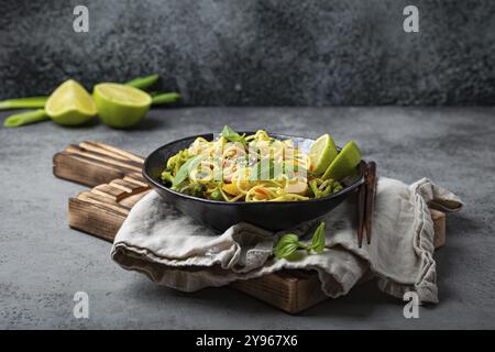 Nouilles végétariennes asiatiques avec légumes et citron vert dans un bol en céramique rustique noir, baguettes en bois sur la planche à découper angle vue sur fond de pierre. COO Banque D'Images