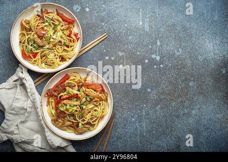 Deux bols avec Chow Mein ou Lo Mein, nouilles sautées chinoises traditionnelles avec viande et légumes, servies avec baguettes vue de dessus sur bleu rustique con Banque D'Images