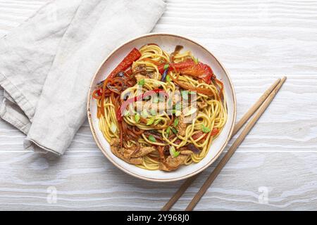 Bol blanc avec Chow Mein ou Lo Mein, nouilles sautées chinoises traditionnelles avec viande et légumes, servies avec baguettes vue de dessus sur blanc rustique w Banque D'Images