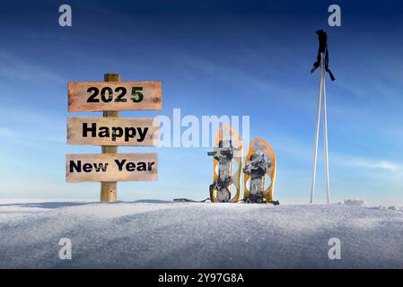 panneau en bois avec texte bonne année 2025 dans la neige à côté de raquettes et bâtons de ski sous le ciel bleu Banque D'Images