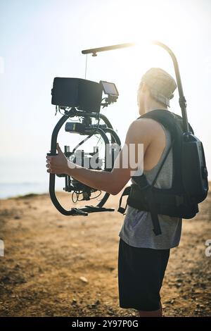 Vidéaste, homme ou caméra vidéo à la plage pour film, production professionnelle ou documentaire de voyage. Caméraman, enregistrez ou filmez dans la nature avec Banque D'Images