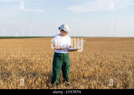 Femme agricultrice portant casquette blanche et t-shirt avec ordinateur portable. Éoliennes en arrière-plan.. Banque D'Images