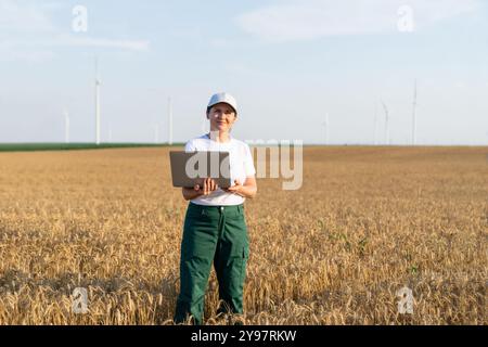 Femme agricultrice portant casquette blanche et t-shirt avec ordinateur portable. Éoliennes en arrière-plan.. Banque D'Images