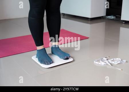 Femme debout sur l'échelle numérique avec ruban à mesurer et tapis de yoga dans le cadre moderne de la maison pour le fitness et la santé Lifestyle Banque D'Images