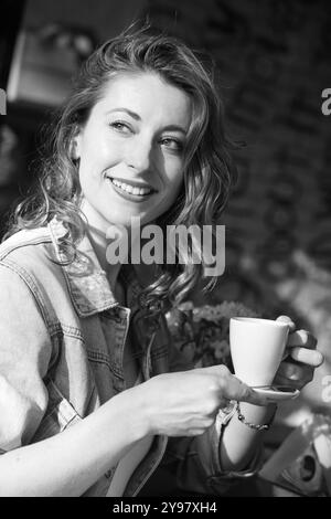 portrait de jolie femme adulte moyenne joyeuse avec des cheveux de gingembre assis à la table dans la cafétéria avec tasse de café à l'extérieur Banque D'Images