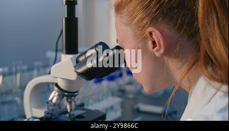 Laboratoire de sciences médicales : gros plan d'une microbiologiste féminine regardant sous microscope, analysant un échantillon de test, développant des médicaments. Brillant scientifique, chimiste utilise des équipements de haute technologie. Recherche scientifique. Banque D'Images