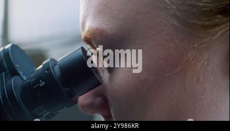 Laboratoire de sciences médicales : une biochimiste féminine regarde au microscope, analyse l'échantillon, développe un vaccin. Microbiologiste professionnel, scientifique utilise des équipements de haute technologie. Médecine. Macro gros plan. Banque D'Images