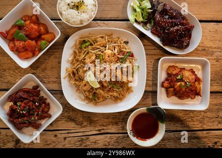 Sélection de plats asiatiques, notamment pad Thai, poulet aigre-doux, ailes de barbecue épicées coréennes et kimchi Banque D'Images