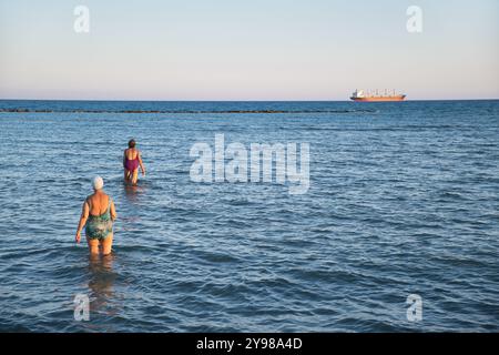 Deux femmes âgées entrant dans les eaux de la plage de Voroklini, larnaca juste avant le coucher du soleil à Chypre Banque D'Images