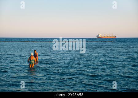 Deux femmes âgées entrant dans les eaux de la plage de Voroklini, larnaca juste avant le coucher du soleil à Chypre Banque D'Images