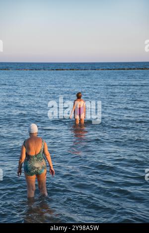 Deux femmes âgées entrant dans les eaux de la plage de Voroklini, larnaca juste avant le coucher du soleil à Chypre Banque D'Images