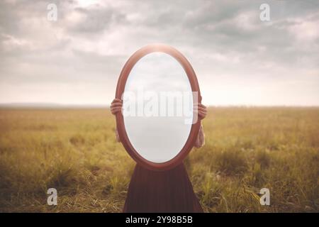 femme se cache tenant un miroir devant son visage ; concept d'introspection la femme se cache tenant un miroir devant son visage ; concept d'introspection Banque D'Images