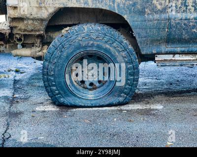 Pneu crevé : Jeep recouverte de boue sur une route asphaltée humide Banque D'Images