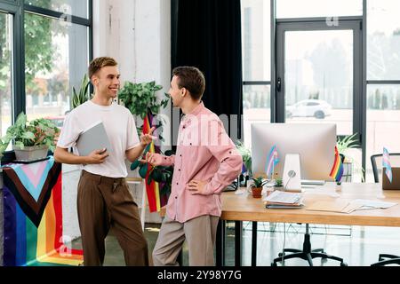 Dans un bureau dynamique, un couple joyeux s'engage dans une conversation animée entouré de drapeaux de fierté. Banque D'Images