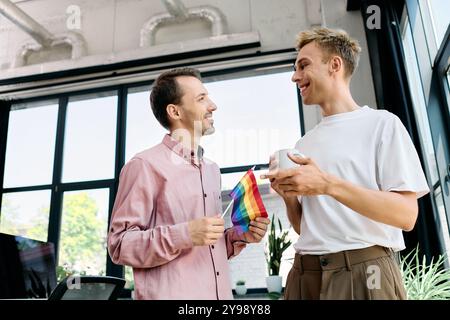 Deux hommes sourient et s'engagent dans la conversation tout en tenant un drapeau arc-en-ciel dans un bureau élégant. Banque D'Images