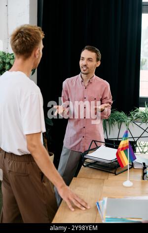 Deux jeunes hommes s'engagent dans une discussion animée, partageant des sourires dans un environnement de bureau élégant. Banque D'Images