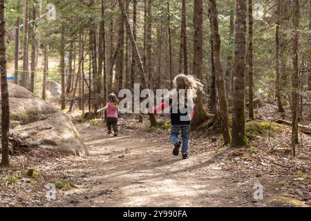 Deux jeunes enfants fuyant la caméra sur un chemin de terre dans une forêt avec de grands arbres Banque D'Images