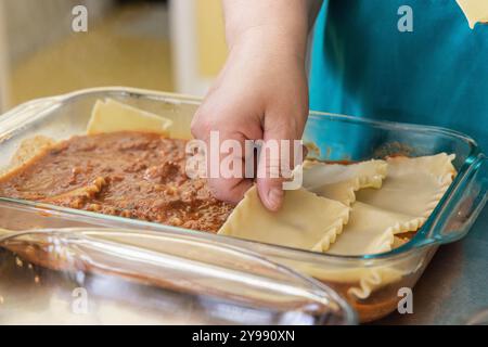 Le chef superpose soigneusement des nouilles lasagnes sur une sauce à la viande, mettant en valeur le processus méticuleux de préparation de ce plat italien classique. Mise au point sélective Banque D'Images