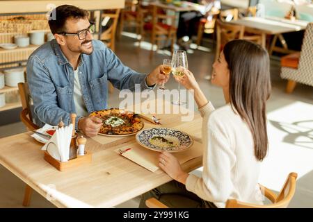 Deux personnes savourent leurs boissons à une table en bois, immergées dans une ambiance de restaurant détendue, tout en étant profondément dans la conversation et les rires. Banque D'Images