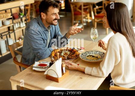 Un couple s'engage dans une conversation animée tout en savourant une délicieuse cuisine dans un restaurant lumineux, partageant des rires et des moments de connexion sur un lei Banque D'Images